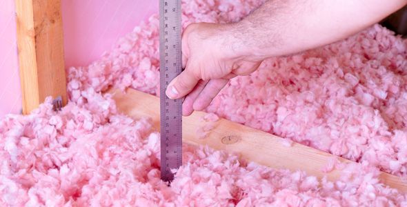 a person is measuring a piece of pink insulation with a ruler