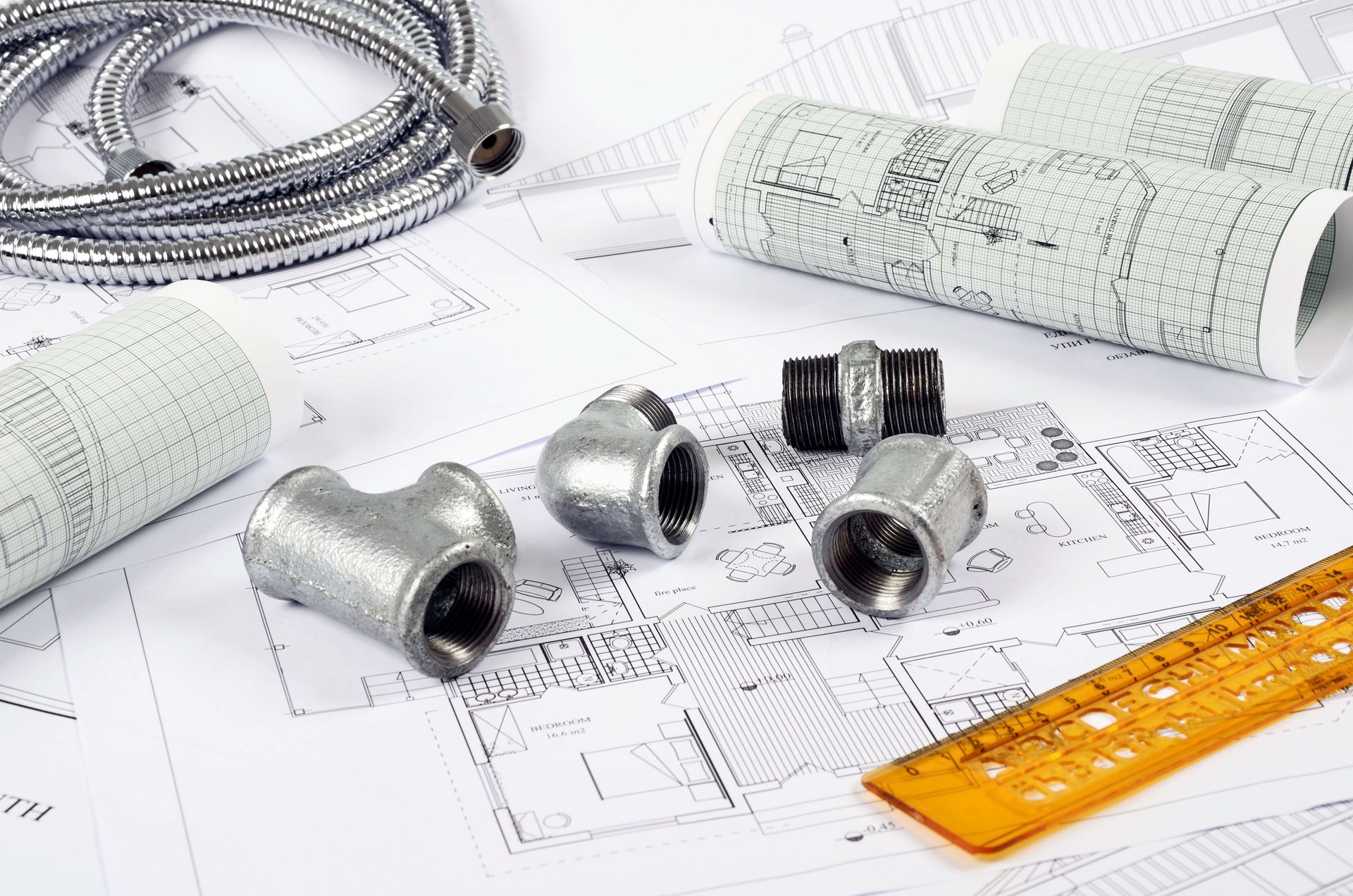 Architectural blueprints with metallic fittings, coiled wire, and an orange ruler on a drafting table