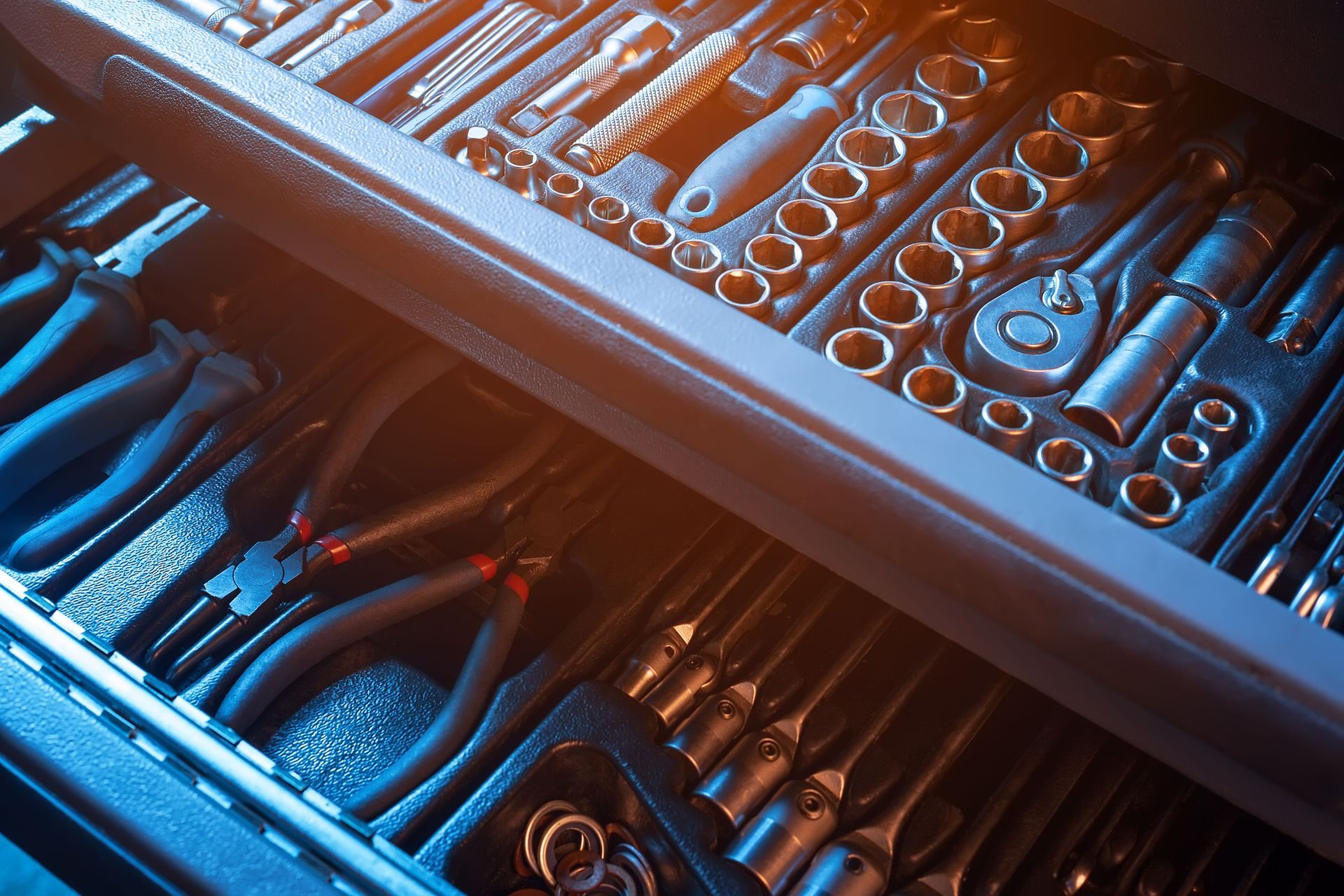 Open metal toolbox with neatly arranged hand tools in blue and orange light