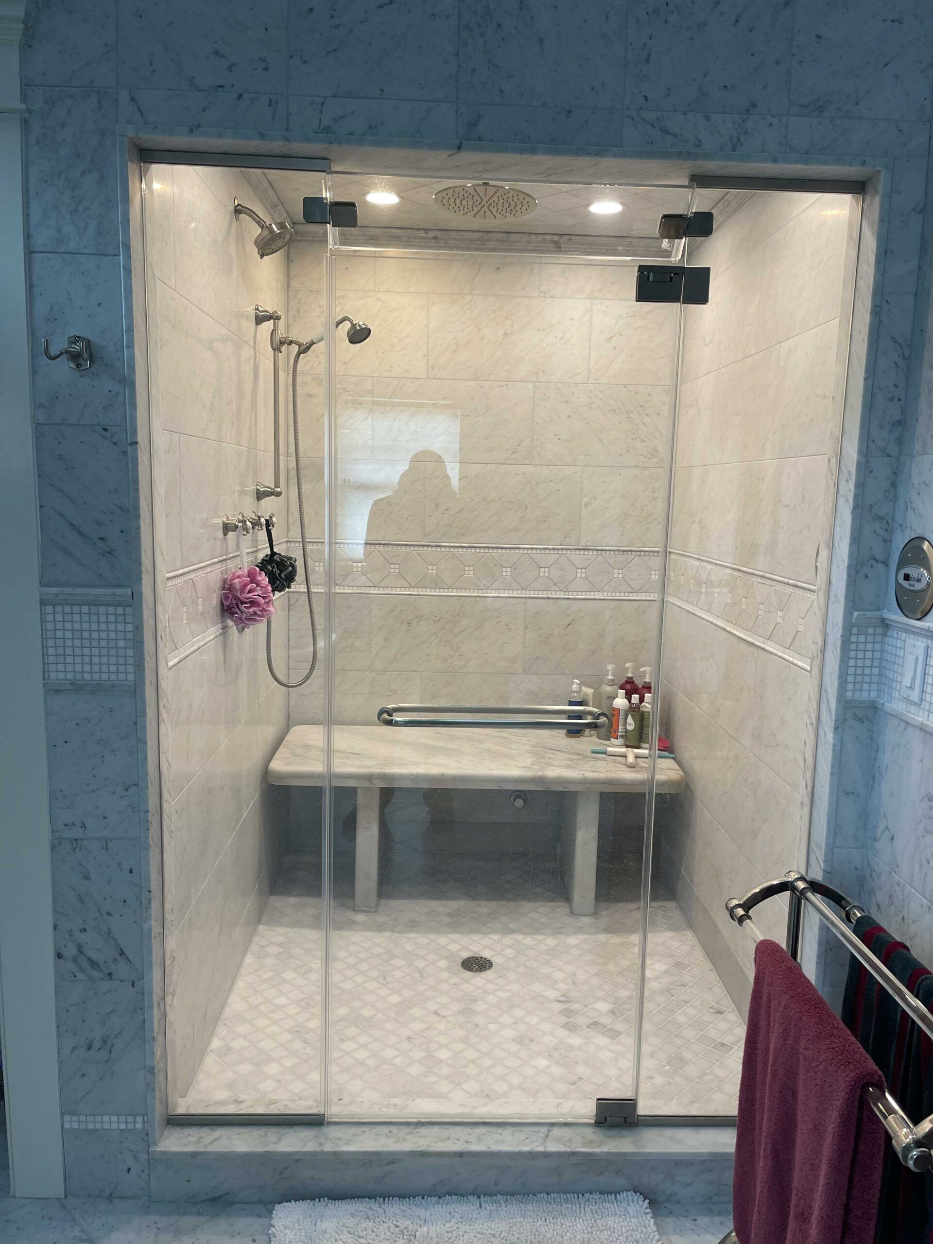 A bathroom with a walk in shower with a bench and a glass door.