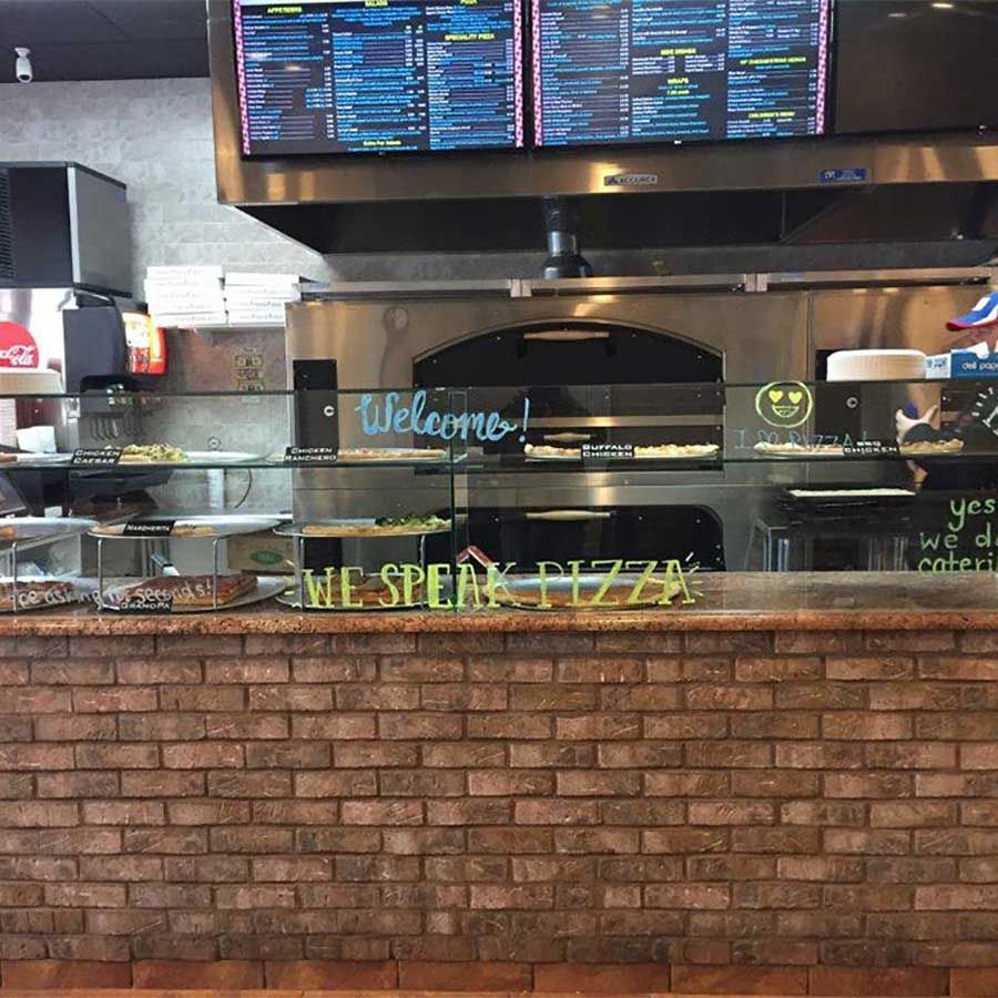 A restaurant with a brick wall and a sign that says we speak pizza
