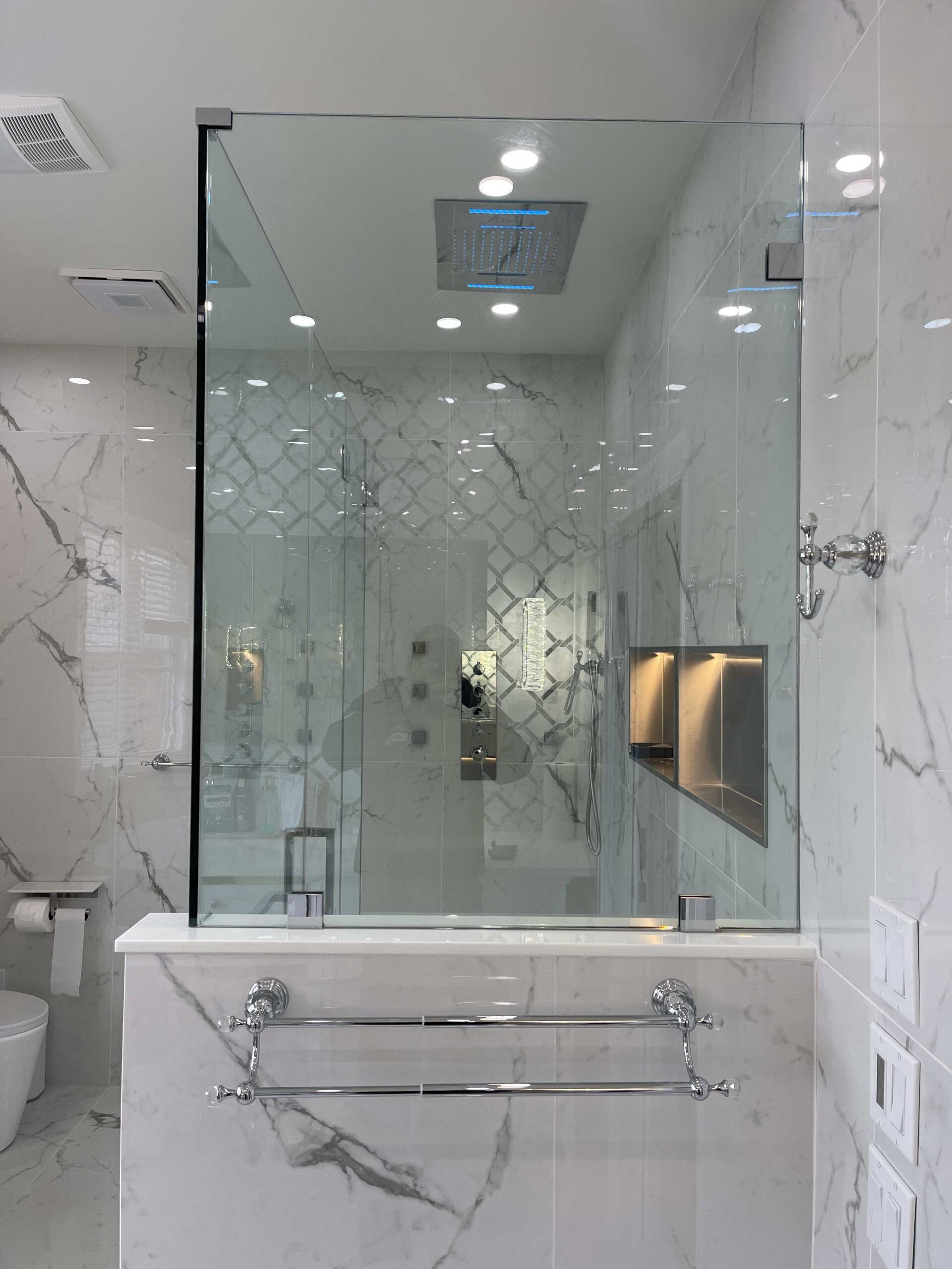 A bathroom with marble walls and a walk in shower with a glass door.