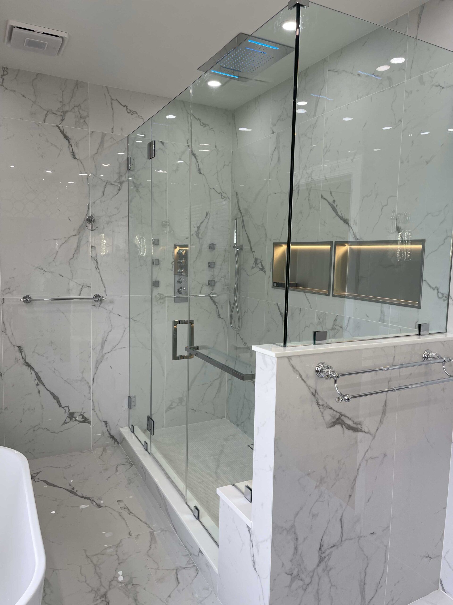 A bathroom with marble walls and a walk in shower with a glass door.