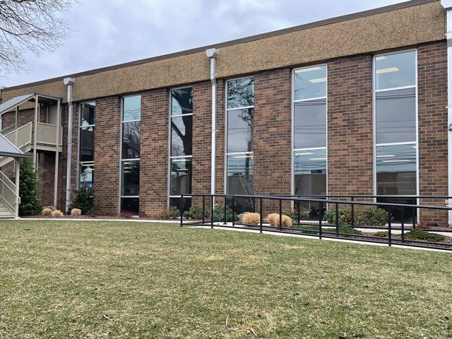 A large brick building with a lot of windows is sitting on top of a lush green field.