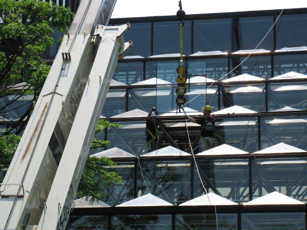 A crane is lifting a large piece of glass on top of a building