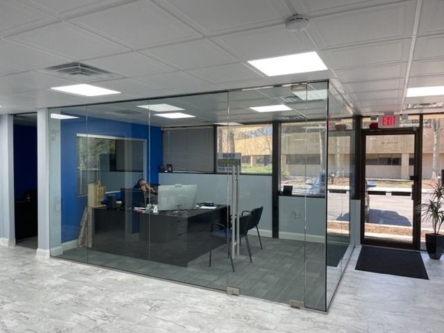 A man is sitting at a desk in a glass office cubicle.