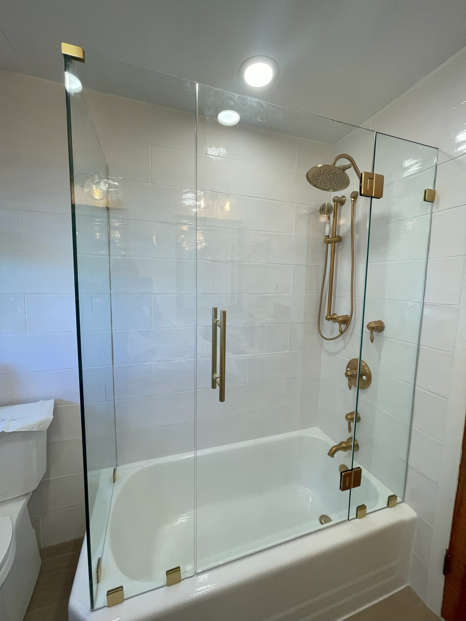 Gold-toned shower fixtures and glass enclosure over a white bathtub in a bathroom.
