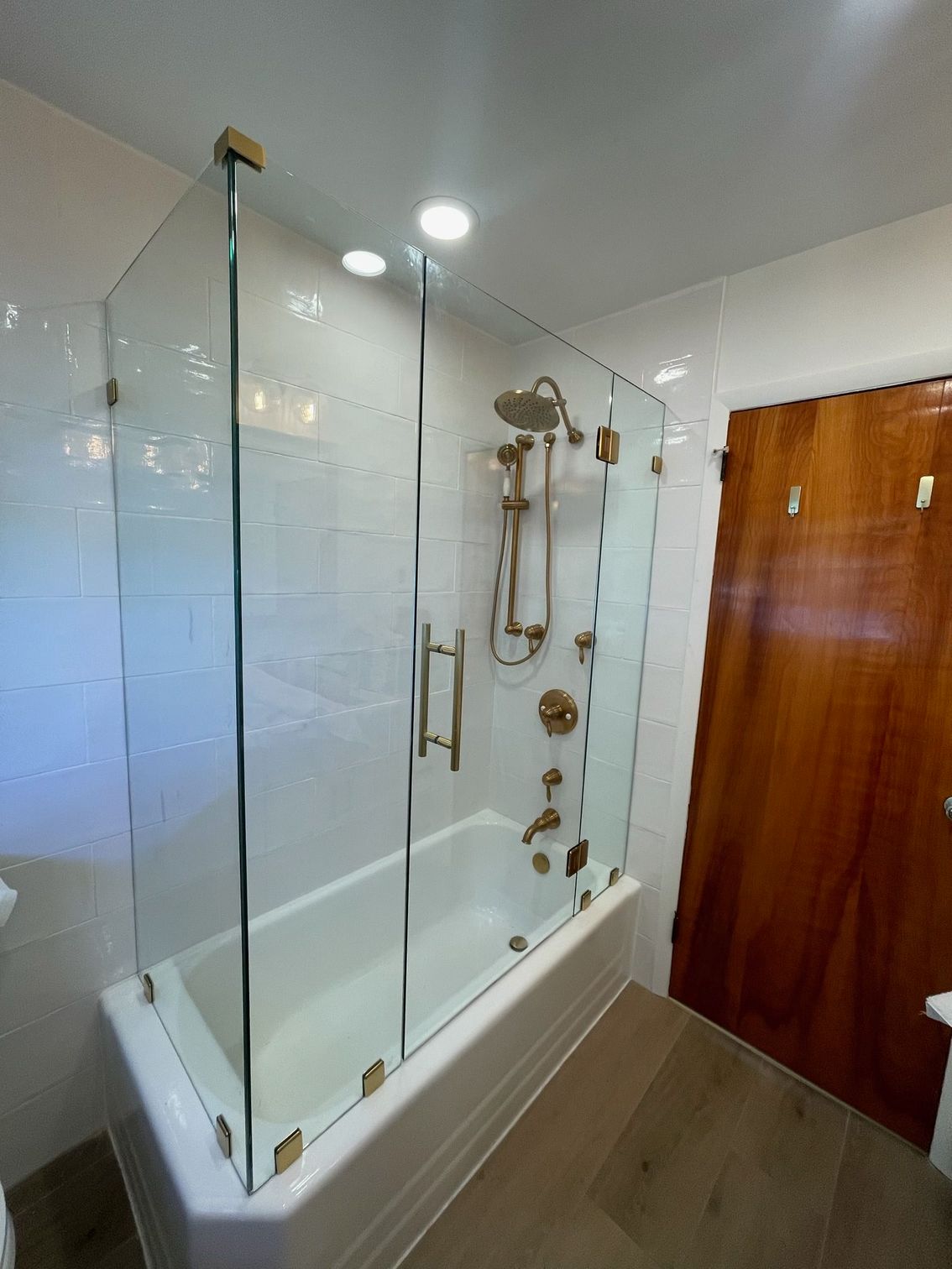 A modern bathroom with a glass shower enclosure, gold fixtures, and a wooden door.