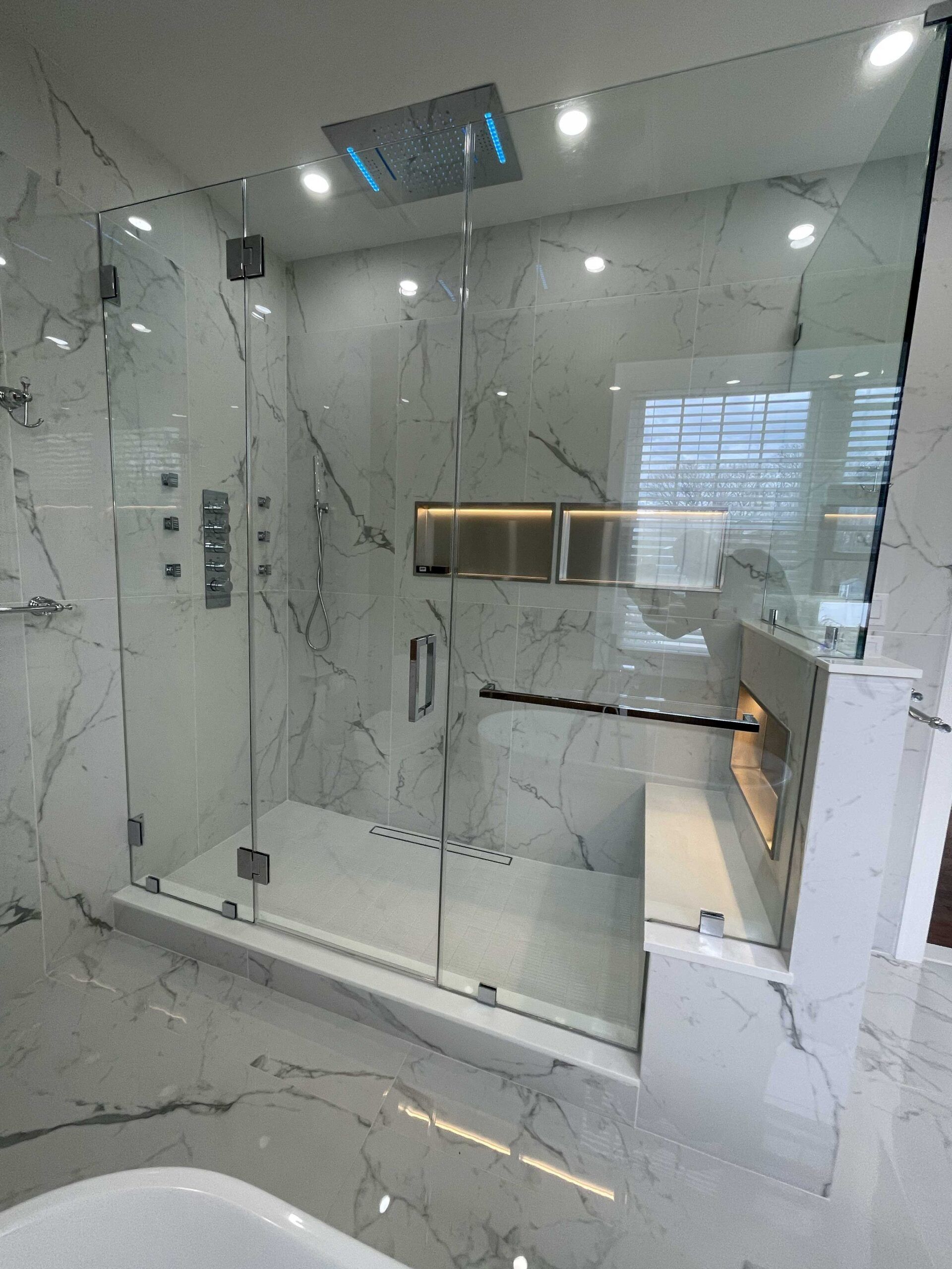 Luxurious marble-tiled shower with glass doors and rain showerhead. Built-in bench and recessed shelves.