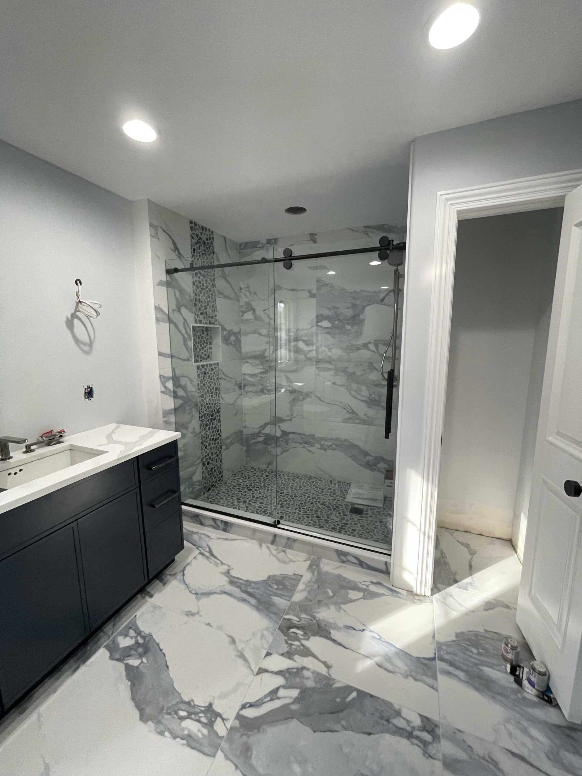 Newly renovated bathroom with marble tile, glass shower, and dark vanity.