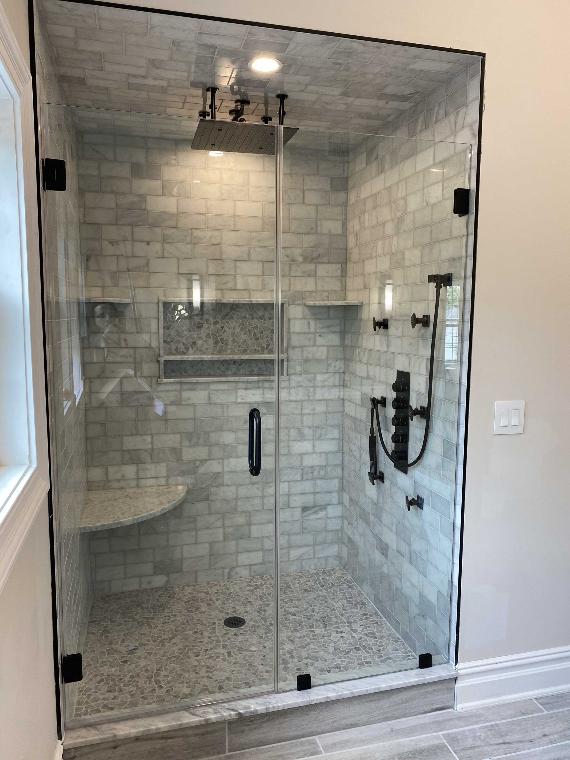 Glass-enclosed shower with black fixtures and marble tile walls, featuring a built-in bench and recessed shelves.