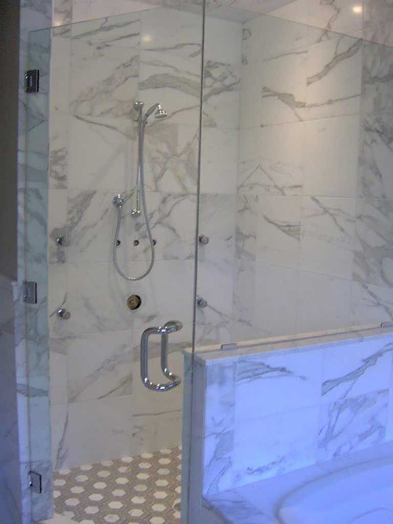 Marble-tiled shower with a glass door and chrome fixtures.