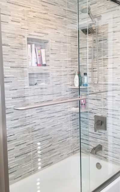 Shower with glass door, tiled walls, built-in shelves holding toiletries, and a tub.