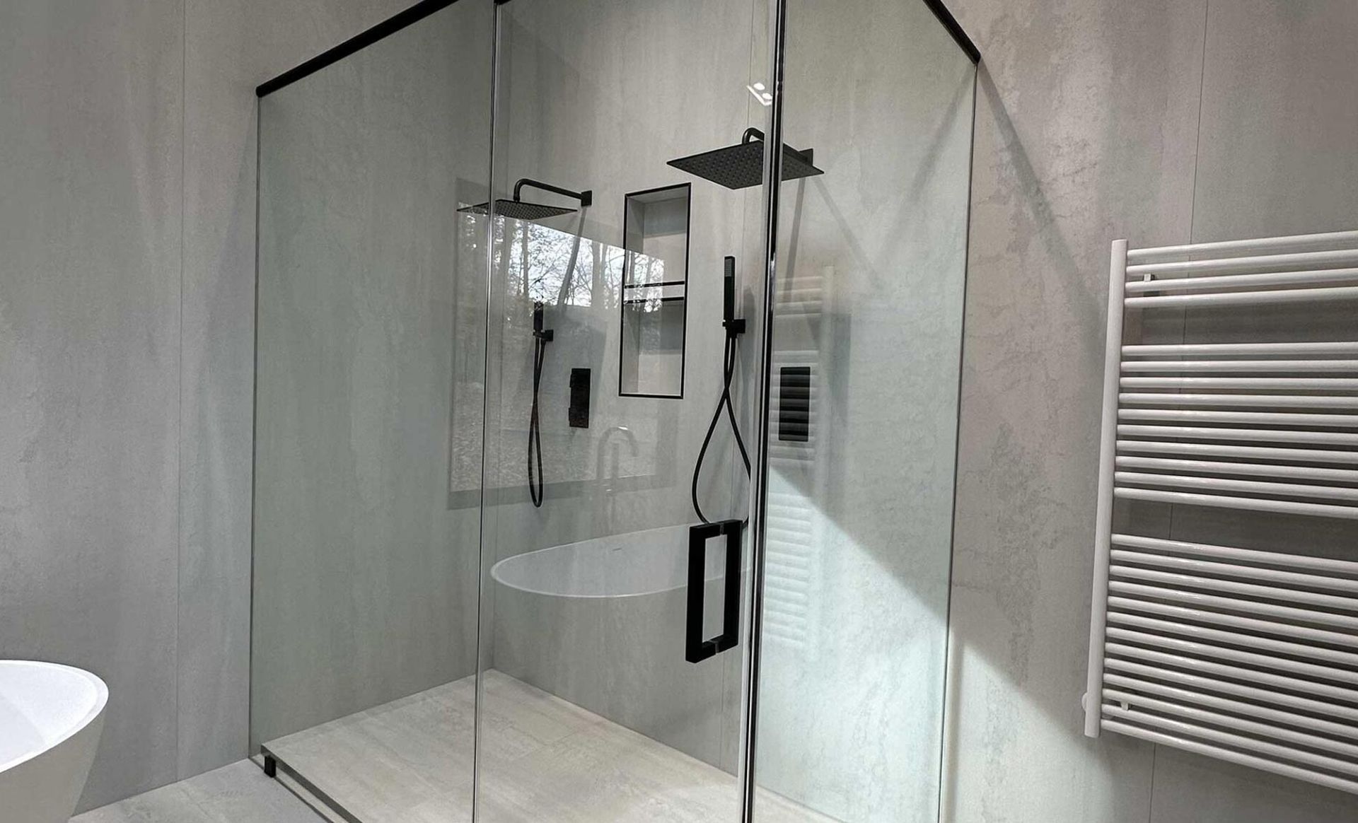 Modern bathroom with glass shower, black fixtures, and white tub. A towel warmer is on the wall.