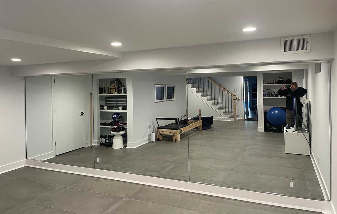 A man is standing in a basement with a large mirror on the wall.