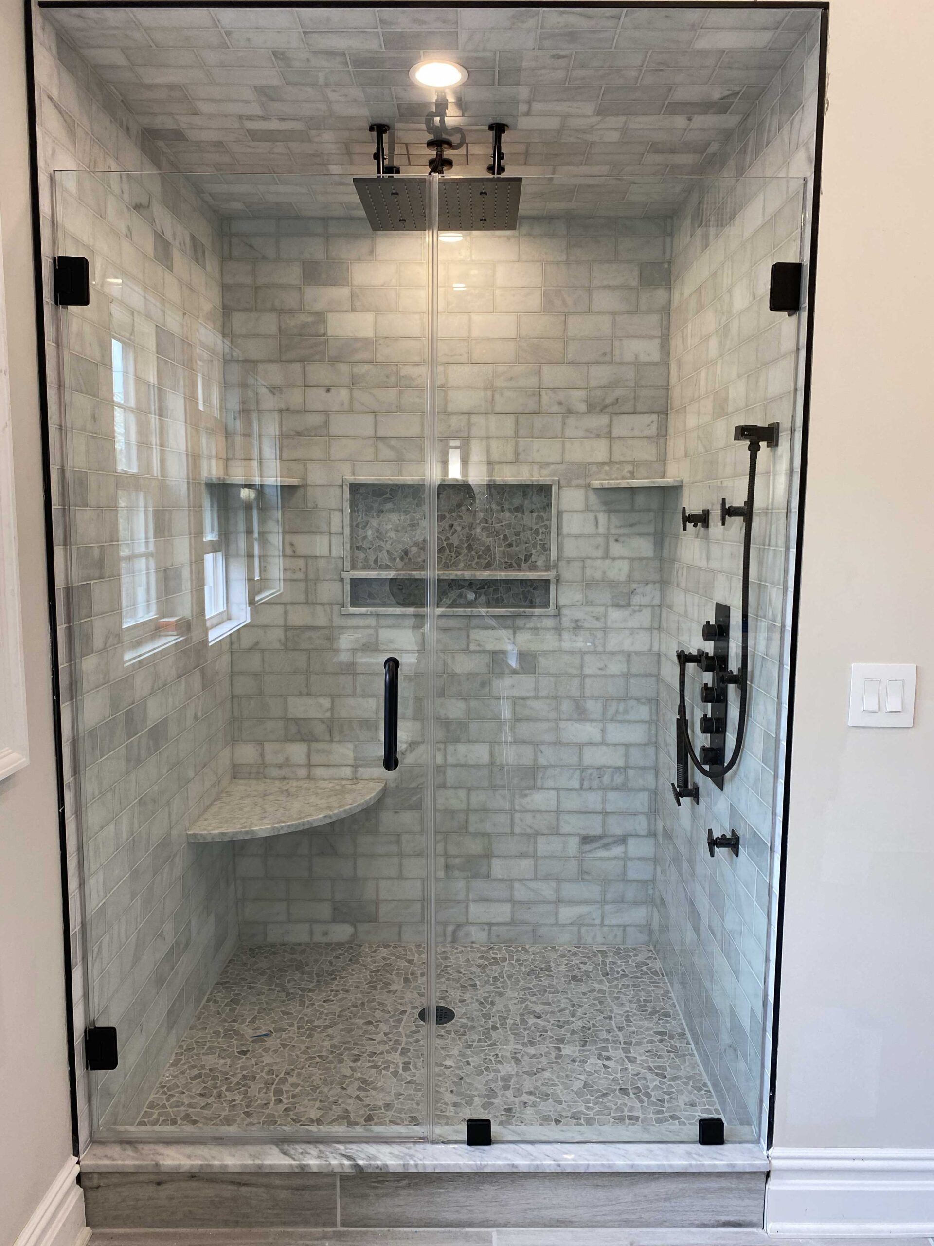 A bathroom with a walk in shower with a glass door and a bench.