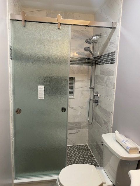 A bathroom with a toilet , shower , and sliding glass door.