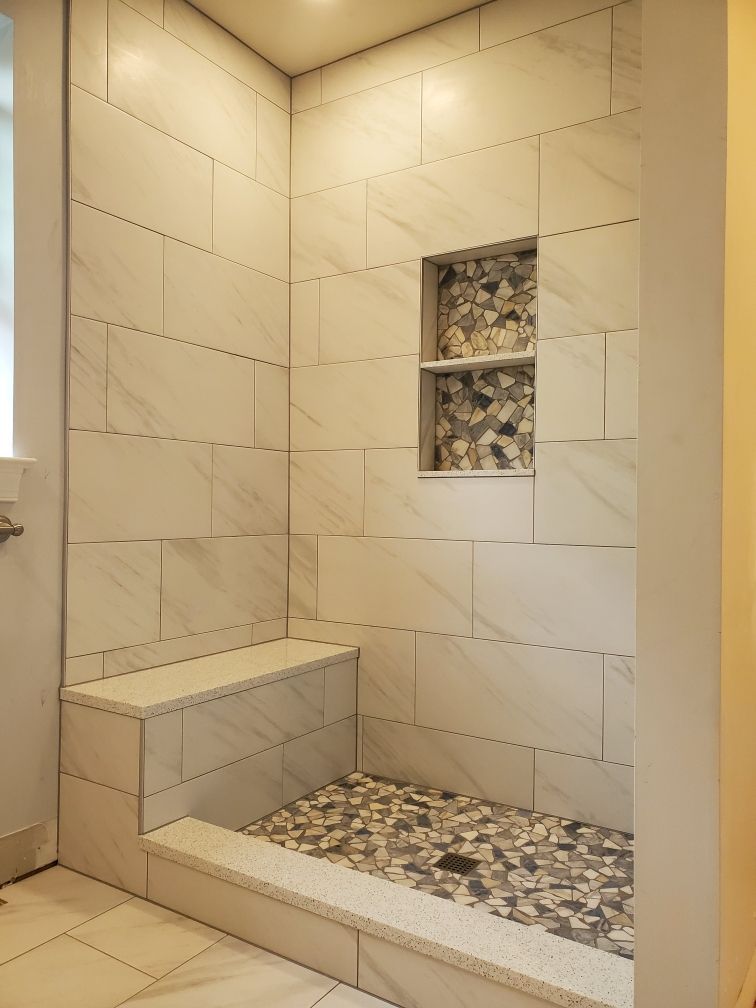 Tiled shower stall with a built-in bench and pebble-tiled floor, featuring a recessed shelf.