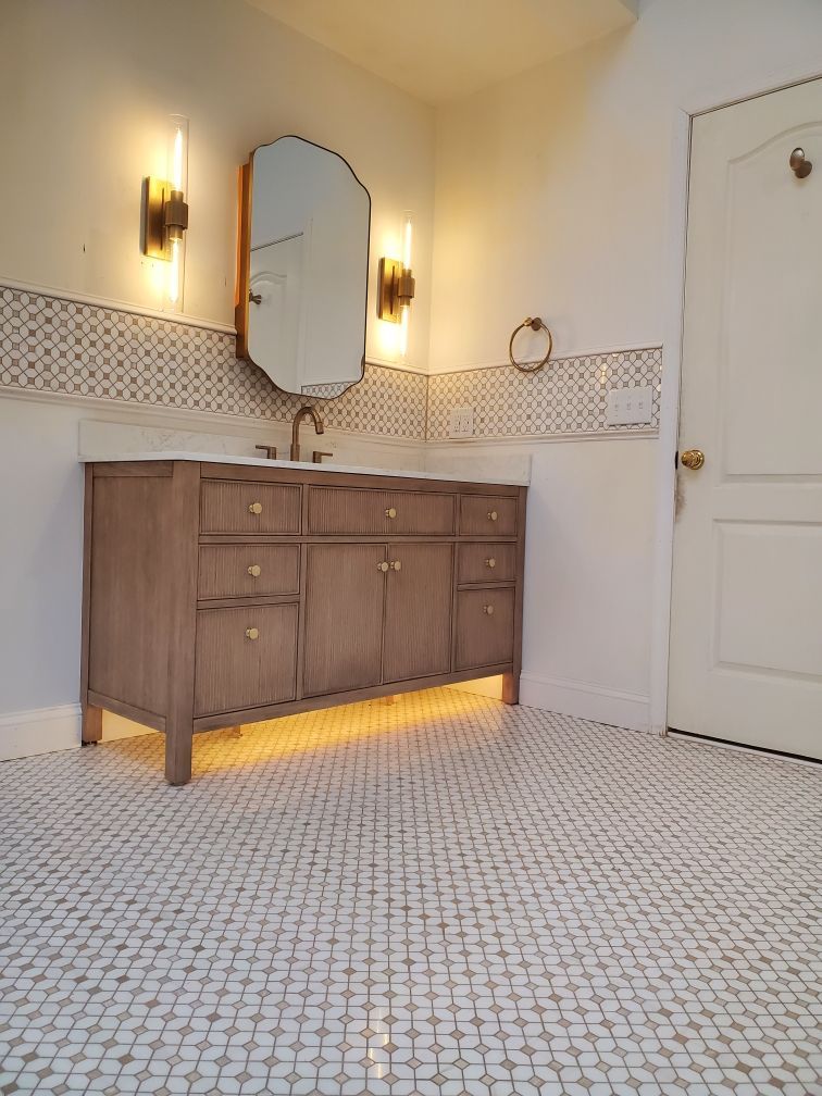 Bathroom with light wood vanity, patterned floor tile, and gold-toned sconces around a mirror.