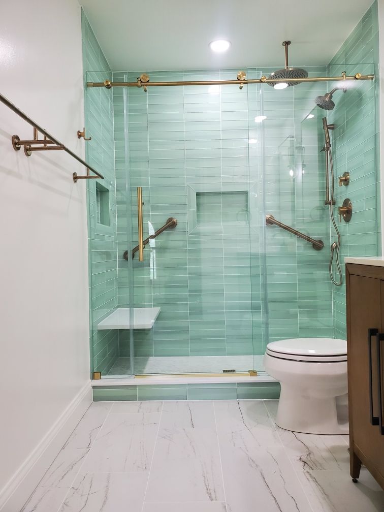 Modern bathroom with a glass shower and teal tile. Includes grab bars and a seat, with a toilet.