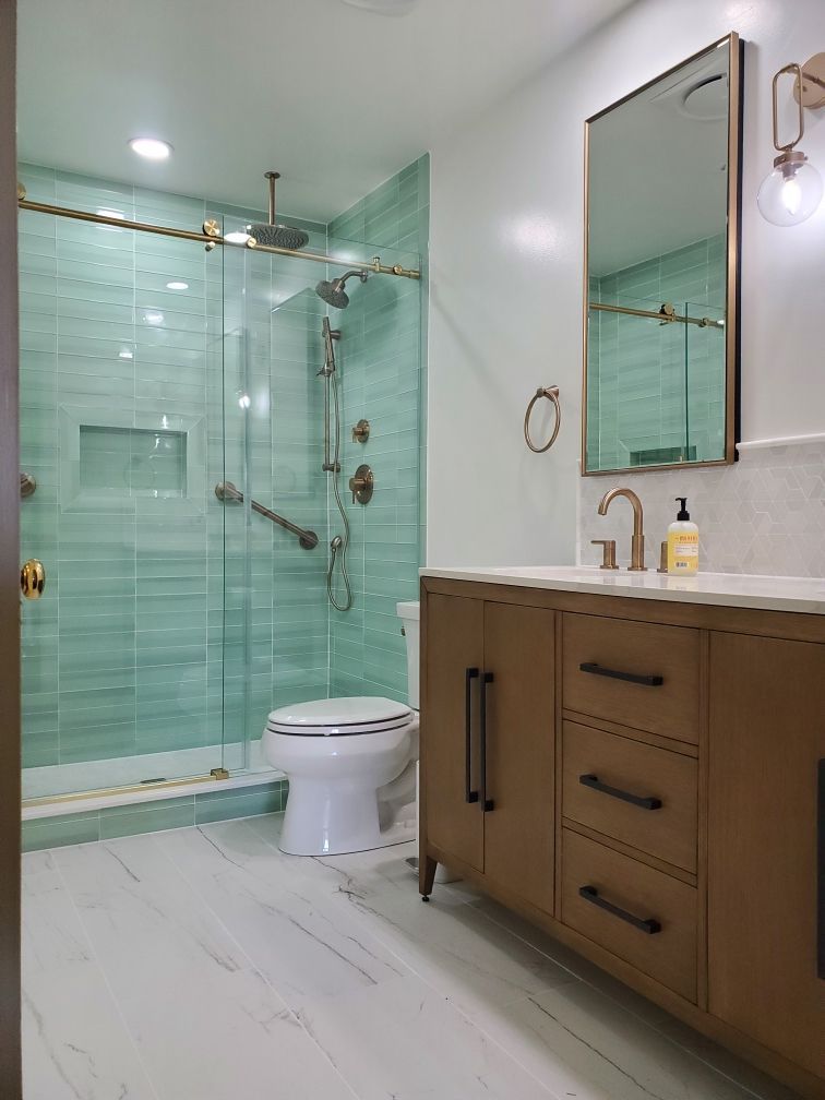 Modern bathroom with teal tiled shower, gold fixtures, and a wooden vanity.