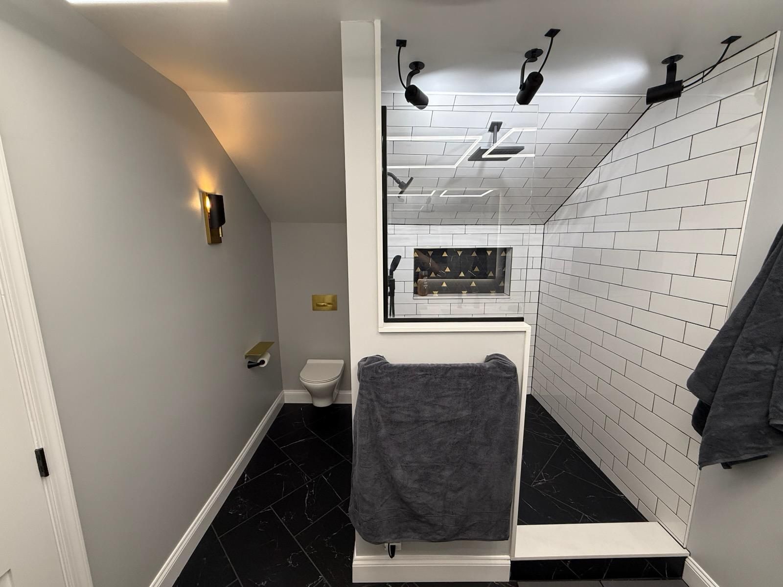 Bathroom with black and white tile. Toilet, shower, towels, and lights are visible.