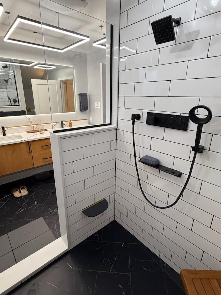 Modern bathroom with black and white tile, glass shower, and black fixtures.
