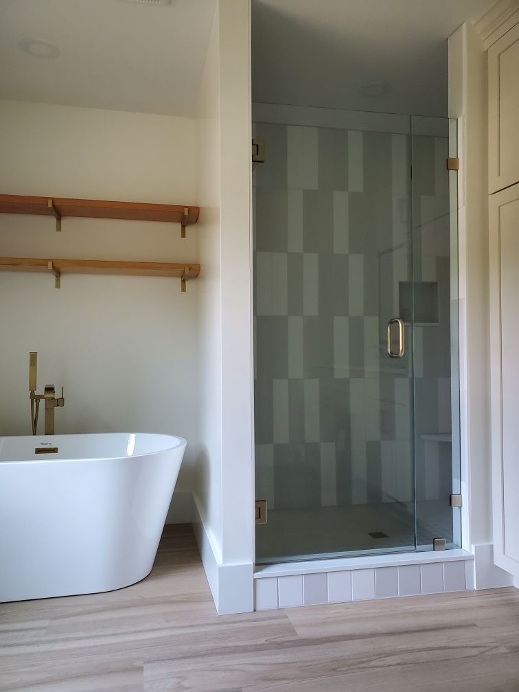 Bathroom with white freestanding tub, glass shower with patterned tiles, wooden shelves, and light wood flooring.