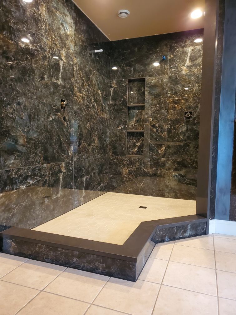 Luxurious shower with dark marbled walls, recessed shelves, and light-colored floor.