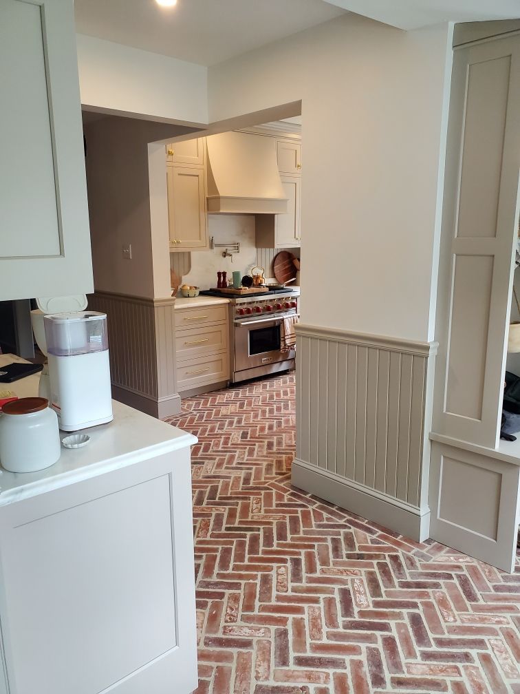 Kitchen with herringbone brick floor, light cabinets, and stainless steel appliances.