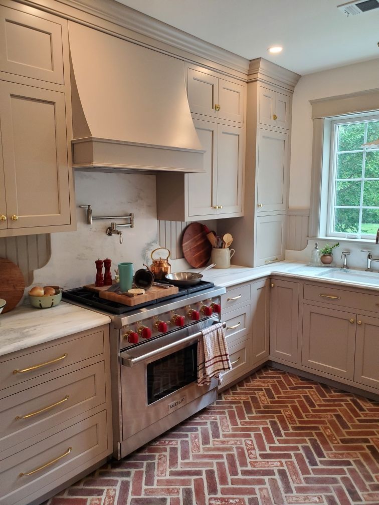 Kitchen with beige cabinets, marble countertops, stainless steel oven, and brick herringbone floor.