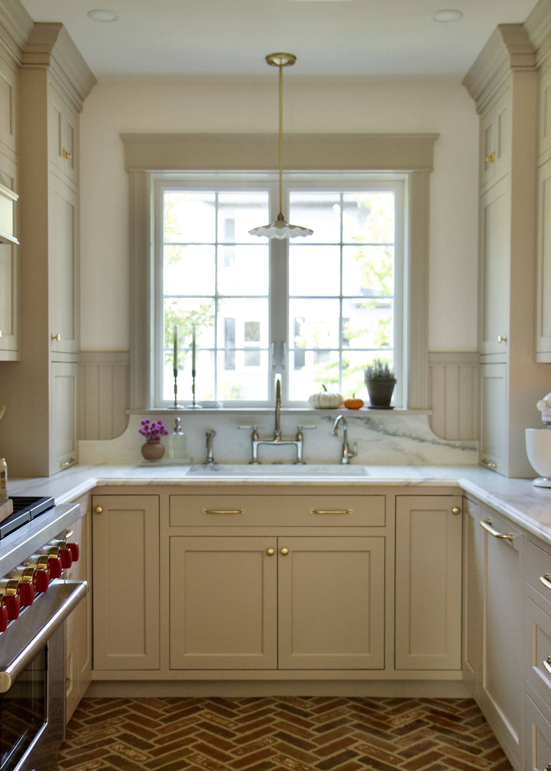 Beige kitchen with a window over a sink and a herringbone-patterned floor.