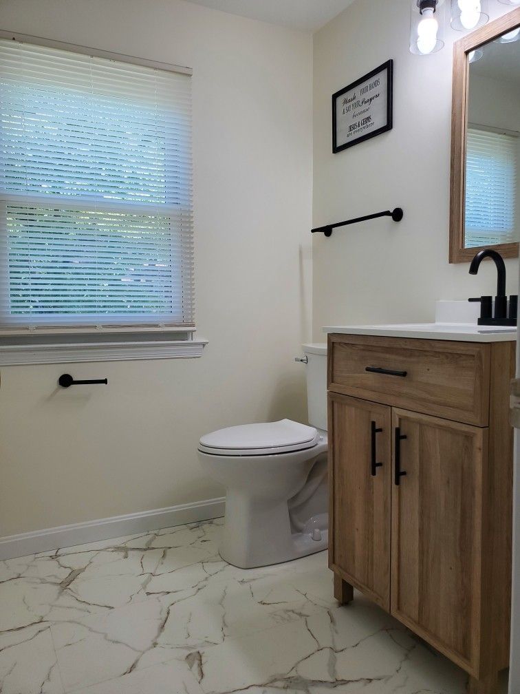 A bathroom with a toilet, sink, mirror and window.