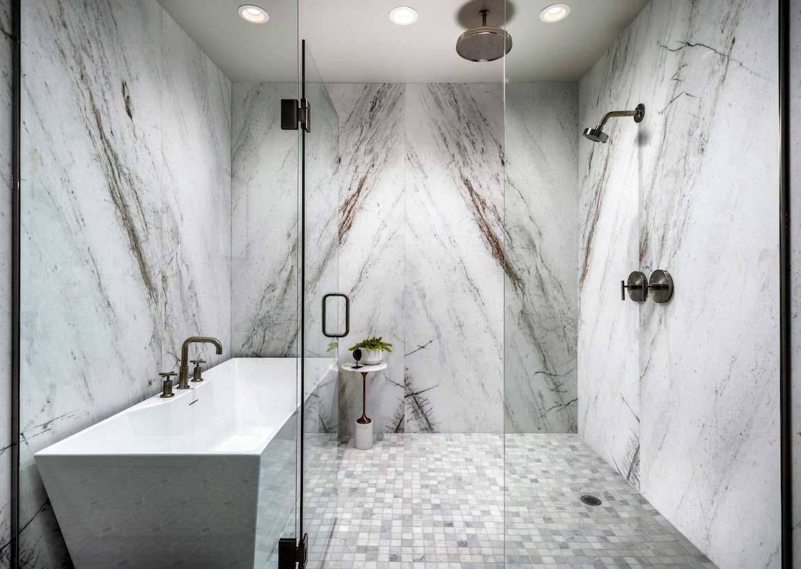 A bathroom with marble walls , a bathtub , and a walk in shower.