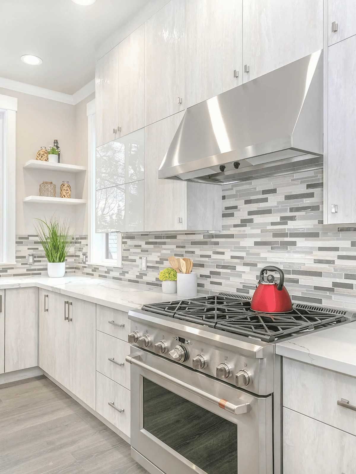 A kitchen with white cabinets , stainless steel appliances , and a red tea kettle on the stove.