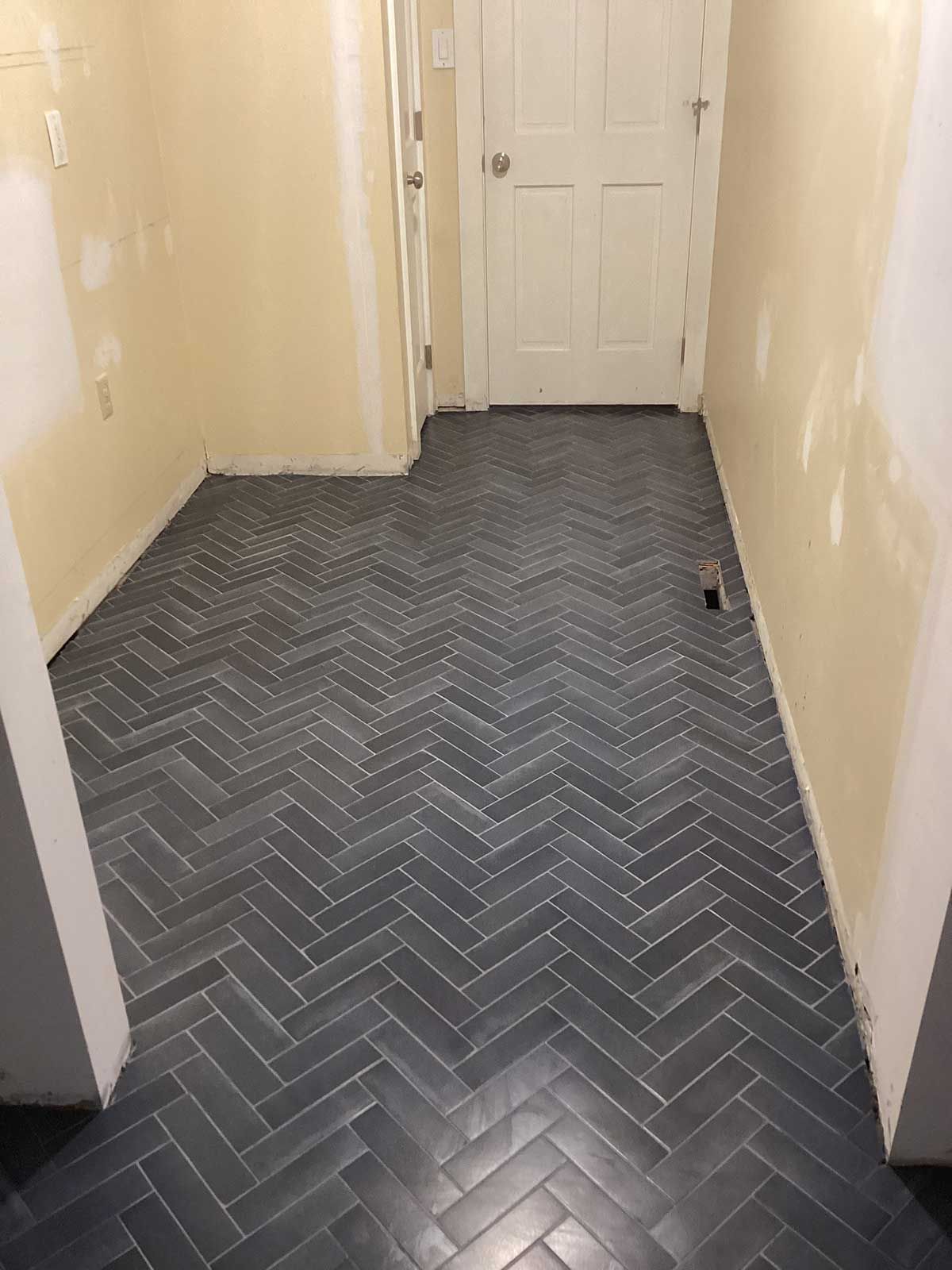 A hallway with a herringbone tile floor and a door.
