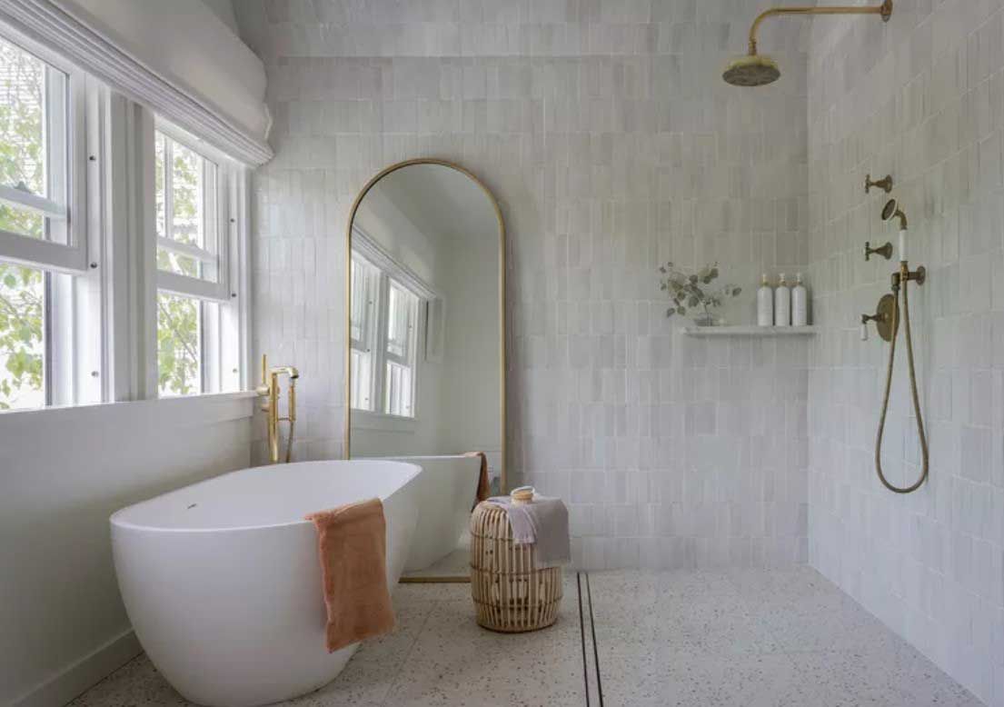 A bathroom with a bathtub , shower , mirror and window.