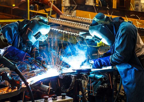 Two welders in blue workwear welding metal in a factory, sparks flying.