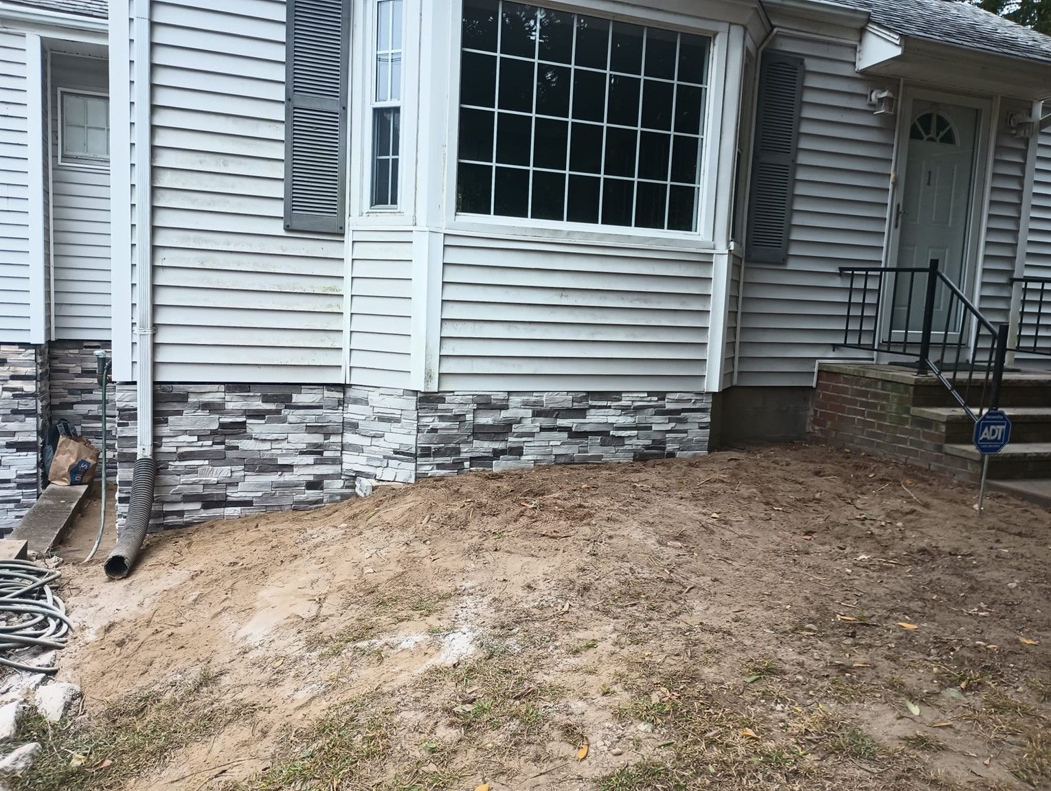 A white house with a stone siding and a large window.