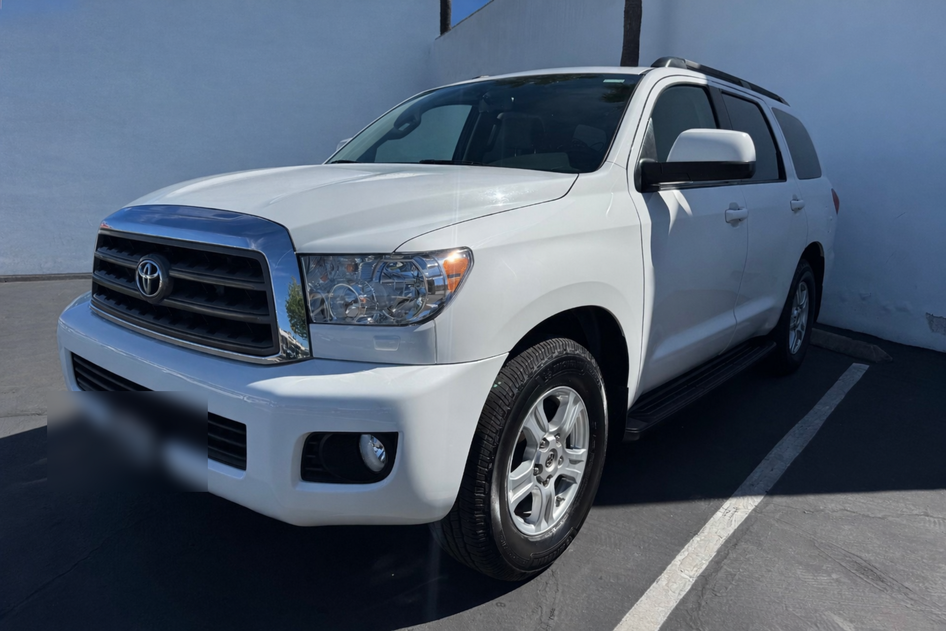 A white Toyota Sequoia SUV parked outdoors against a white wall.