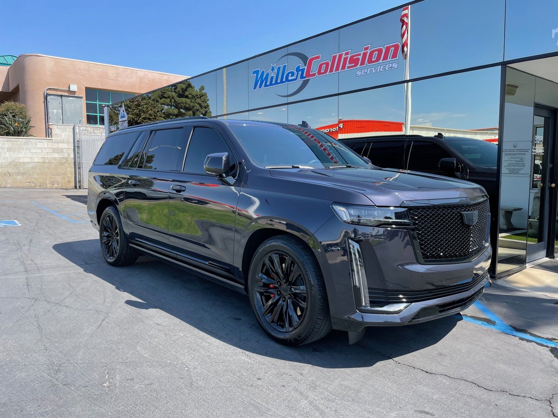 A dark gray Cadillac Escalade parked in front of a Miller Collision building on a sunny day.