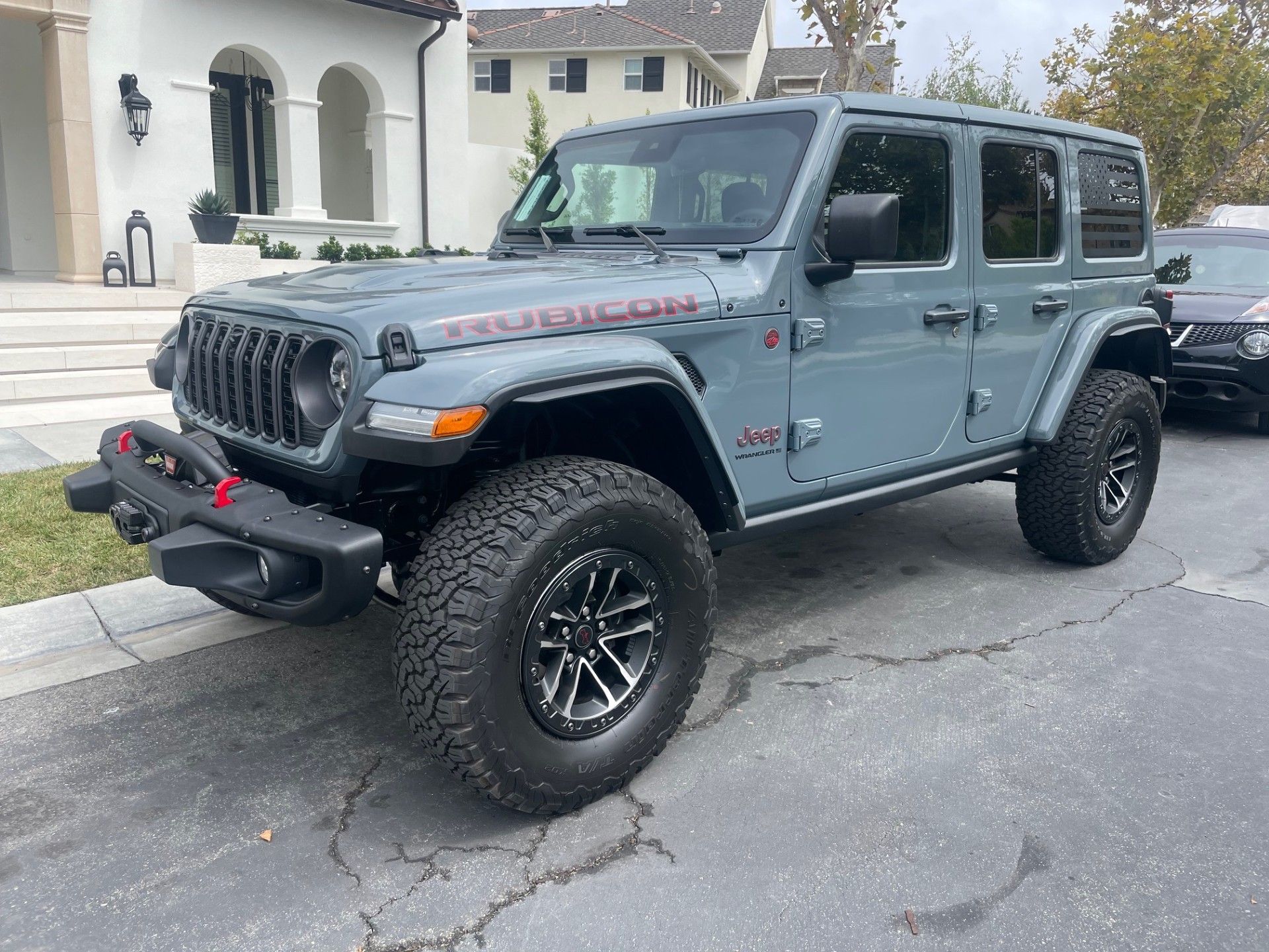 A gray Jeep Wrangler Rubicon parked in a residential driveway with a white house in the background.