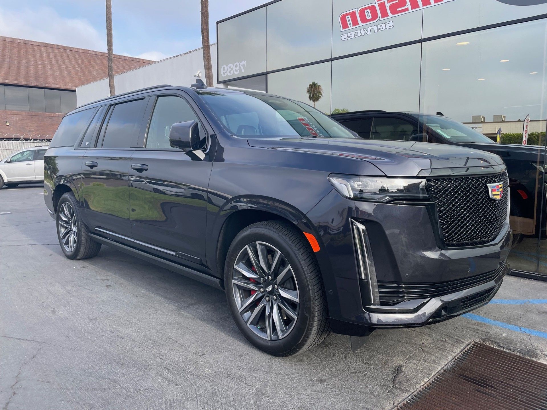 A dark gray Cadillac Escalade parked in front of a car dealership on a sunny day.