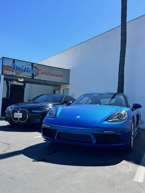 A blue Porsche and a black BMW parked in front of a Miller Collision building under a clear blue sky.