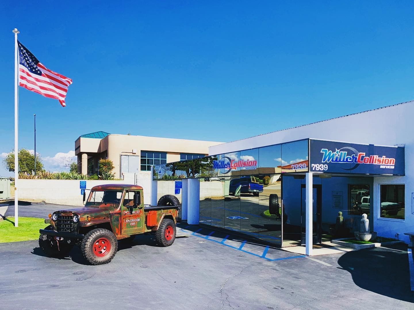 Rustic pickup truck parked outside a business with an American flag. Blue sky.