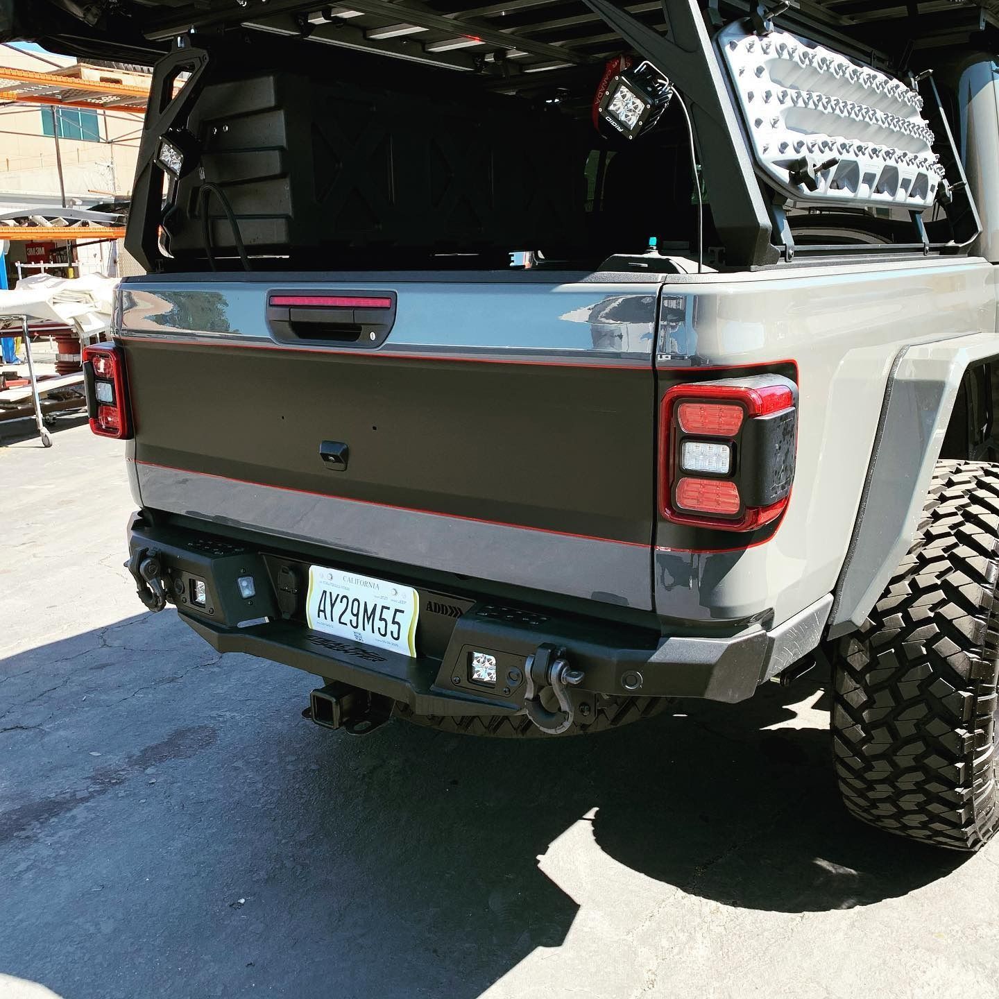 Gray Jeep Gladiator truck with black modifications, large tires, and a roof rack, parked outdoors.