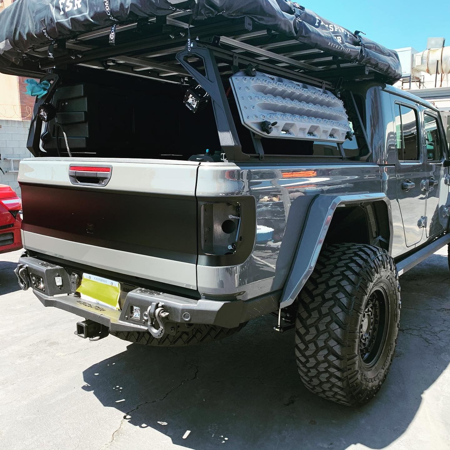 Gray lifted Jeep truck with black off-road accessories, large tires, and a roof-top tent.