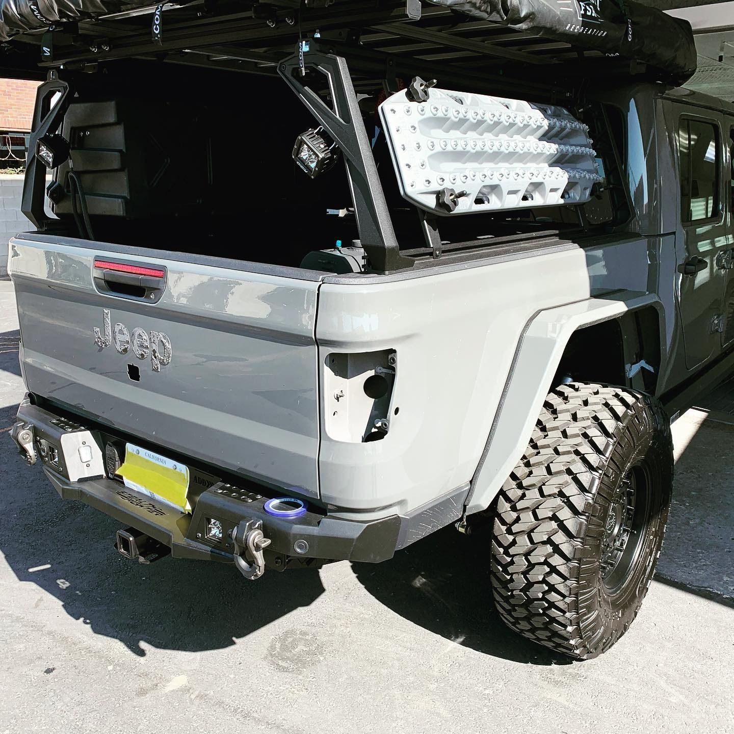 Gray Jeep Gladiator pickup truck with off-road modifications, including a rear bumper and large tires.