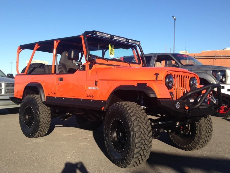 Orange Jeep Wrangler with black accents, large tires, and roll cage, parked outside.