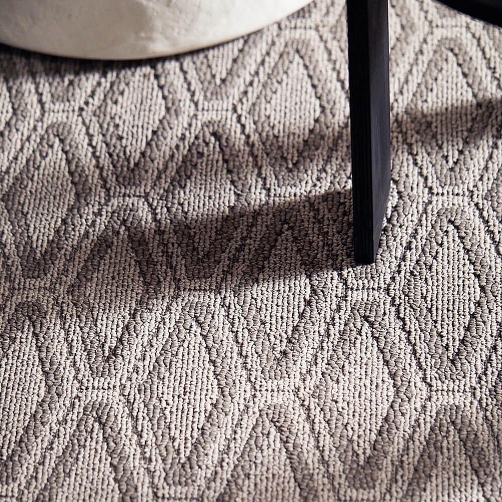 A close up of a rug on a floor next to a chair.